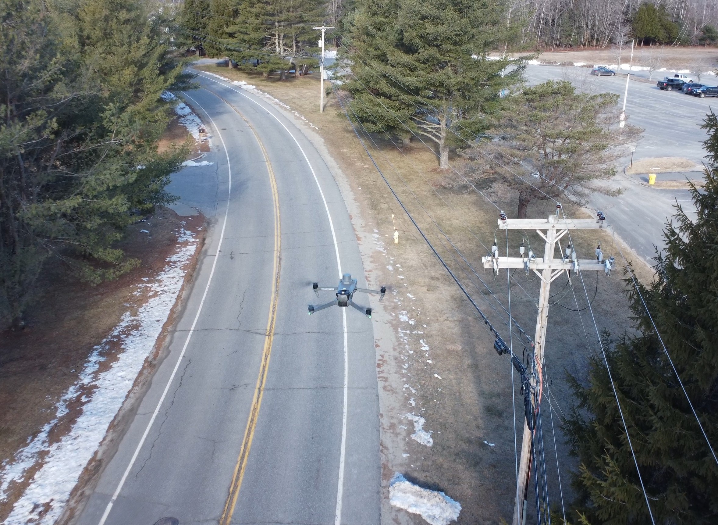 Aerial Image of a road lined with evergreen trees and a powerlines with a drone over them