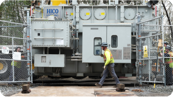 utility worker walking in front of a large transformer